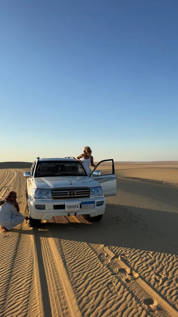A vehicle stopped on the sand before the dunes