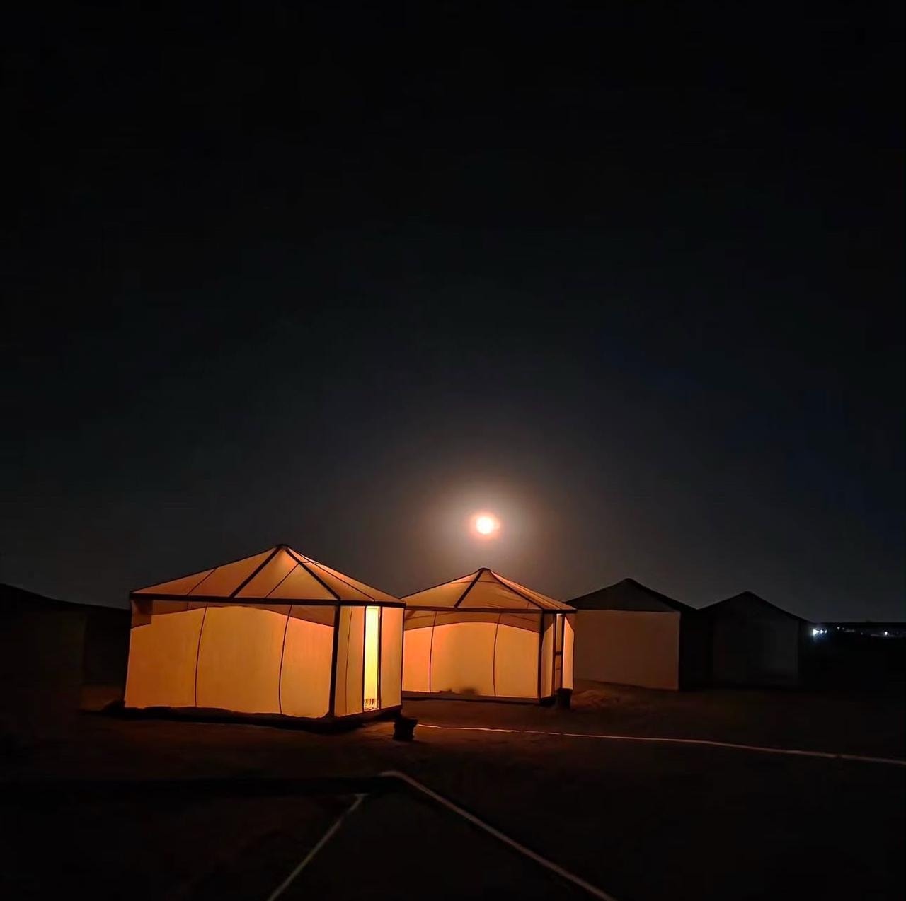Lit tents among the dunes under a full moon